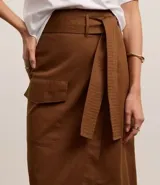 Pollera midi marrón de corte evasé, confeccionada en sarga de algodón. Presenta cintura con trabillas, cinturón con lazo, bolsillo cargo con solapa y encaje delantero.