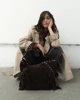 Cartera tipo hobo de gamuza color marrón oscuro, con diseño boho que incluye flecos laterales y detalles de tachas metálicas en el asa y el cuerpo. Cuenta con un compartimento principal amplio y forro interior.