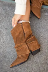Botas de caña media confeccionadas en gamuza color marrón, con diseño slouchy y cierre lateral. Presentan una silueta de punta fina y taco cuña oculto.