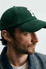 Gorra de seis paneles confeccionada en tejido de algodón, color verde oscuro, con parche frontal de letra P en color crema y ajuste posterior.