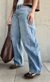 Jean de denim celeste de corte barrel, tiro bajo, con roturas y detalles desgastados en la rodilla.