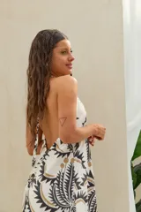 Vestido largo color blanco con estampado de palmeras en tonos negros y dorados, con escote halter y diseño fluido sin mangas.