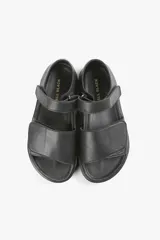 Sandalia plana negra de cuero, con tiras anchas cruzadas y ajuste con velcro.