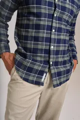Camisa de manga larga confeccionada en tejido de franela con estampado de cuadros en tonos azul marino y verde. Presenta cuello abotonado, cierre frontal con botones y un bolsillo en el pecho con el logo bordado de la marca.