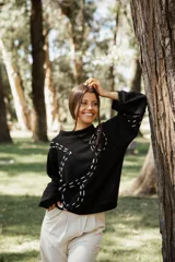 Buzo de punto color negro con diseño de bordado en hilo crudo que forma líneas curvas decorativas. Presenta cuello redondo, mangas largas con caída relajada y corte holgado.