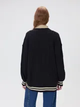 Cardigan de tejido de punto con diseño de ochos, corte oversize y mangas largas con puños acanalados. Presenta un escote en V con solapas en contraste, cierre frontal con botones y dos bolsillos delanteros con bordes en contraste. El diseño incluye detalles de rayas en los puños y en el ruedo.