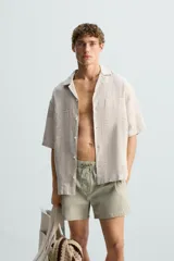 Bañador de hombre color verde claro con finas rayas blancas verticales (efecto seersucker). Tiene cintura elástica ajustable con cordón verde, bolsillos laterales y un bolsillo trasero de vivo.
