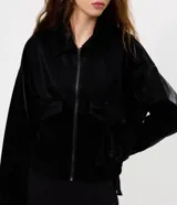 Campera bomber de poliuretano texturizado en color negro, con cuello camisero, cierre frontal, bolsillos aplicados en el pecho y ruedo elástico.