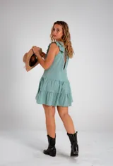 Vestido corto color verde agua, con escote en V profundo, volados en los hombros y detalle de encaje vertical en el frente. Presenta una falda con cortes horizontales que le otorgan movimiento.