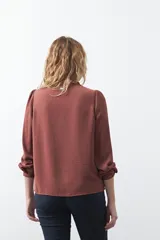 Camisa negra de corte clásico con escote en V, botones frontales y mangas largas con puños. Presenta detalles de recortes calados en la zona de los hombros.