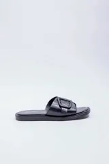 Sandalias planas Paddock modelo Amelias, de color negro con textura efecto cocodrilo. Presentan una tira ancha en el empeine decorada con una hebilla grande cuadrada del mismo material y tono.