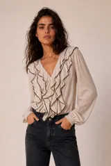 Camisa de manga larga color blanco, con escote en V y volados frontales ribeteados en negro, y puños elásticos fruncidos.