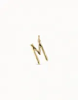Dije con forma de letra M, bañado en oro, con diseño inspirado en un clavo. Pieza artesanal de estilo minimalista.