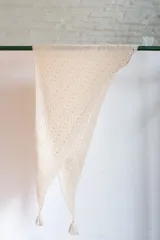 Chal triangular tejido a mano en lana de alpaca natural color crudo, con diseño calado y terminación con borlas.