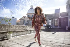 Campera impermeable con capucha y cierre frontal, con estampado de hojas en tonos marrones y ocres. Tiene bolsillos laterales ocultos y cordón ajustable en la cintura.