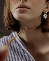 Choker marrón de gamuza con dije de doble aro entrelazado, uno liso y otro con incrustaciones de strass. Los extremos del choker tienen detalles de cuentas doradas.