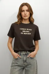 Remera de algodón color marrón oscuro, de corte holgado, con cuello redondo y mangas cortas. Presenta un estampado tipográfico en el pecho con la frase 'I ONLY WANT DRAMA IN MOVIES' en color crema.