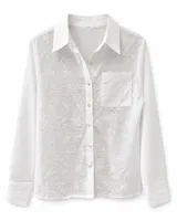 Camisa blanca de manga larga con diseño de bordados florales y ojalillos. Cuenta con cuello camisero, cierre frontal de botones, un bolsillo aplicado en el pecho y puños simples.