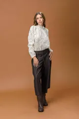 Camisa de encaje color crudo, con cuello alto con volados, mangas largas abullonadas y puños elásticos.