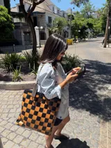 Bolso tipo tote de cuero trenzado a mano con diseño de damero en colores marrón y beige. Cuenta con doble asa trenzada y forro interior.