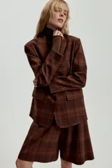 Blazer Zara de cuello solapa y manga larga, con estampado de cuadros en tonos marrones y rojizos. Presenta cierre frontal con dos botones y bolsillos delanteros con solapa.