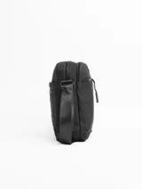 Morral de diseño compacto y funcional, confeccionado en tela resistente color negro. Cuenta con múltiples compartimentos con cierre, incluyendo bolsillos frontales y traseros para una organización óptima. Incluye una correa ajustable para llevar al hombro o cruzado, con detalle de etiqueta de marca en la parte inferior.