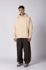 Buzo canguro color marrón con capucha, confeccionado en frisa de algodón. Presenta un diseño gráfico estampado en el frente con texto y logo circular, bolsillo tipo canguro y puños acanalados.