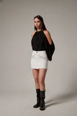 Minifalda de jean blanca con tachas y strass aplicados en la parte delantera, tiro alto y ruedo desmechado.