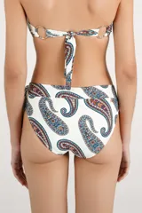 Calzón de bikini tipo faja de tiro alto, color blanco con estampado paisley en tonos azul, rojo y mostaza. Cuenta con una argolla metálica decorativa y un lazo lateral.