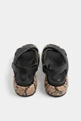 Sandalia de cuero ovino color negro, con tiras acolchadas cruzadas en el empeine y tira trasera con hebilla ajustable. Cuenta con una plataforma plana revestida con estampado de piel de serpiente.