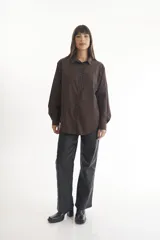 Camisa marrón de corte clásico, con cuello abotonado, mangas largas y bolsillo frontal.