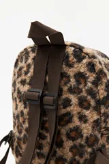 Mochila compacta con estampado animal print de textura suave y esponjosa. Cuenta con un bolsillo frontal con cierre, correas ajustables y asa superior en color marrón.