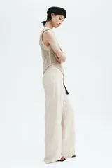 Pantalón sastrero de tiro alto en color beige, con perneras amplias y raya marcada en la parte delantera y trasera. Cuenta con cierre de cremallera, botón oculto y corchete, además de bolsillos decorativos insertados.
