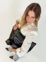 Cartera tote de cuero genuino color negro, con costuras visibles a contratono, asas dobles para hombro, parche frontal con logo grabado y charms colgantes en forma de estrella y mini monedero.