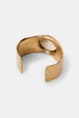 Pulsera rígida de metal con acabado texturizado y labrado en tono dorado, con una aplicación central circular incrustada de cristales negros brillantes.