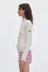 Cardigan de punto color marfil con cierre frontal completo, cuello alto y detalles de rayas en contraste en cuello, puños y ruedo. Presenta diseño de ochos verticales.