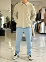 Campera de gabardina beige de corte boxy fit, con cuello camisero, cierre frontal de cremallera blanca y bolsillos laterales ribeteados.