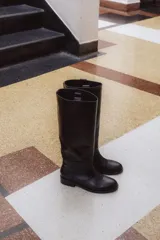 Bota de caña alta color marrón, confeccionada en cuero vacuno con forro y plantilla de cuero. Tiene suela de goma negra y un diseño de caña ancha.