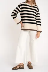 Sweater de punto a rayas horizontales negras y crudas, con cuello redondo y mangas largas. Tiene ribete marrón en puños y ruedo.