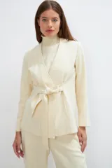 Chaqueta corta color beige, entallada, con escote en V, manga larga y bolsillos escondidos. Cierre frontal con lazo fijo. Confeccionada en lana fina sin teñir. Diseño exclusivo de Don Baez.