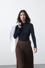 Polera de tejido de punto con textura calada y diseño de líneas verticales acanaladas. Presenta cuello alto y mangas largas con puños delicados, de silueta entallada.