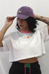 Gorra tipo baseball de color gris con efecto desgastado, presenta un detalle circular en color rosa y verde en la parte frontal.