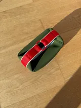 Neceser de neopreno color borgoña, con cierre superior y forro interior. Tiene un asa de mano con una franja azul y blanca.