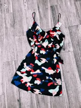 Vestido corto negro con estampado abstracto en tonos celeste, rosa y rojo, con breteles finos y corte evasé.