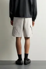 Bermuda cargo color negro de corte relaxed fit, confeccionada en tejido de algodón con elasticidad y efecto lavado. Cuenta con cintura elástica ajustable con cordón, bolsillos frontales y bolsillos laterales tipo cargo con solapa en las perneras.