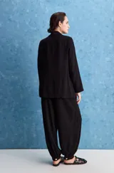 Pantalón negro de tiro alto y calce holgado, con pierna amplia, bolsillos laterales y puños ajustados con botones en los tobillos.