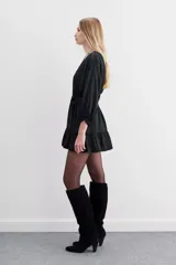 Vestido corto de estilo cruzado, color negro, con mangas largas abullonadas, puños elásticos y volado en el ruedo. Presenta un diseño de jacquard con corazones y cierre frontal con botones metálicos.