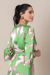 Vestido midi cruzado de satén estampado en tonos verde, blanco y rosa. Tiene lazo en la cintura, mangas 3/4 acampanadas y falda irregular con volados.