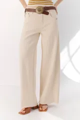 Pantalón de algodón color crema, de corte palazzo, tiro alto y ruedo desflecado. Incluye cinturón marrón con hebilla circular dorada.