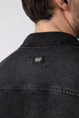 Chaqueta de jean negro desgastado, de corte recto, con cuello clásico, cierre frontal con botones y bolsillo en el pecho. Confeccionada en denim de algodón de 12 onzas.